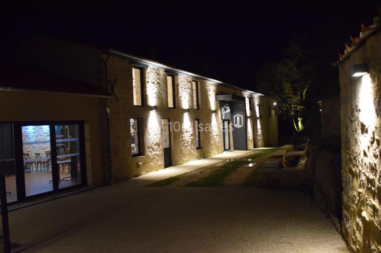 Façade en pierre d'un bâtiment éclairé la nuit, avec une entrée principale et une salle visible à travers une baie vitrée.