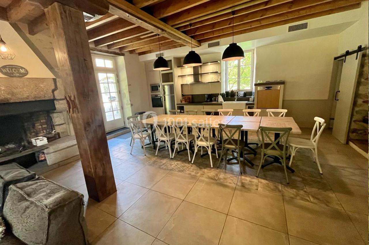 Salle à manger avec une grande table entourée de chaises, une cuisine ouverte et une cheminée en pierre.