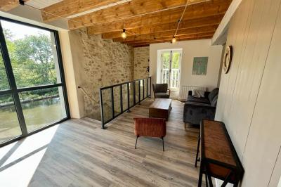 Groupe de personnes rassemblées sur une terrasse en bord de rivière, entourée de verdure et décorée de guirlandes lumineuses.