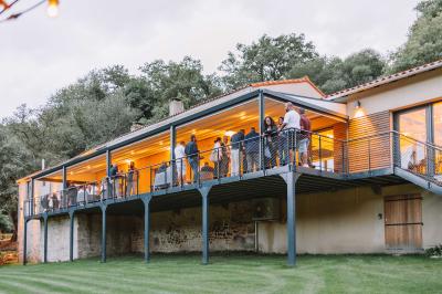 Groupe de personnes rassemblées sur une terrasse en bord de rivière, entourée de verdure et décorée de guirlandes lumineuses.