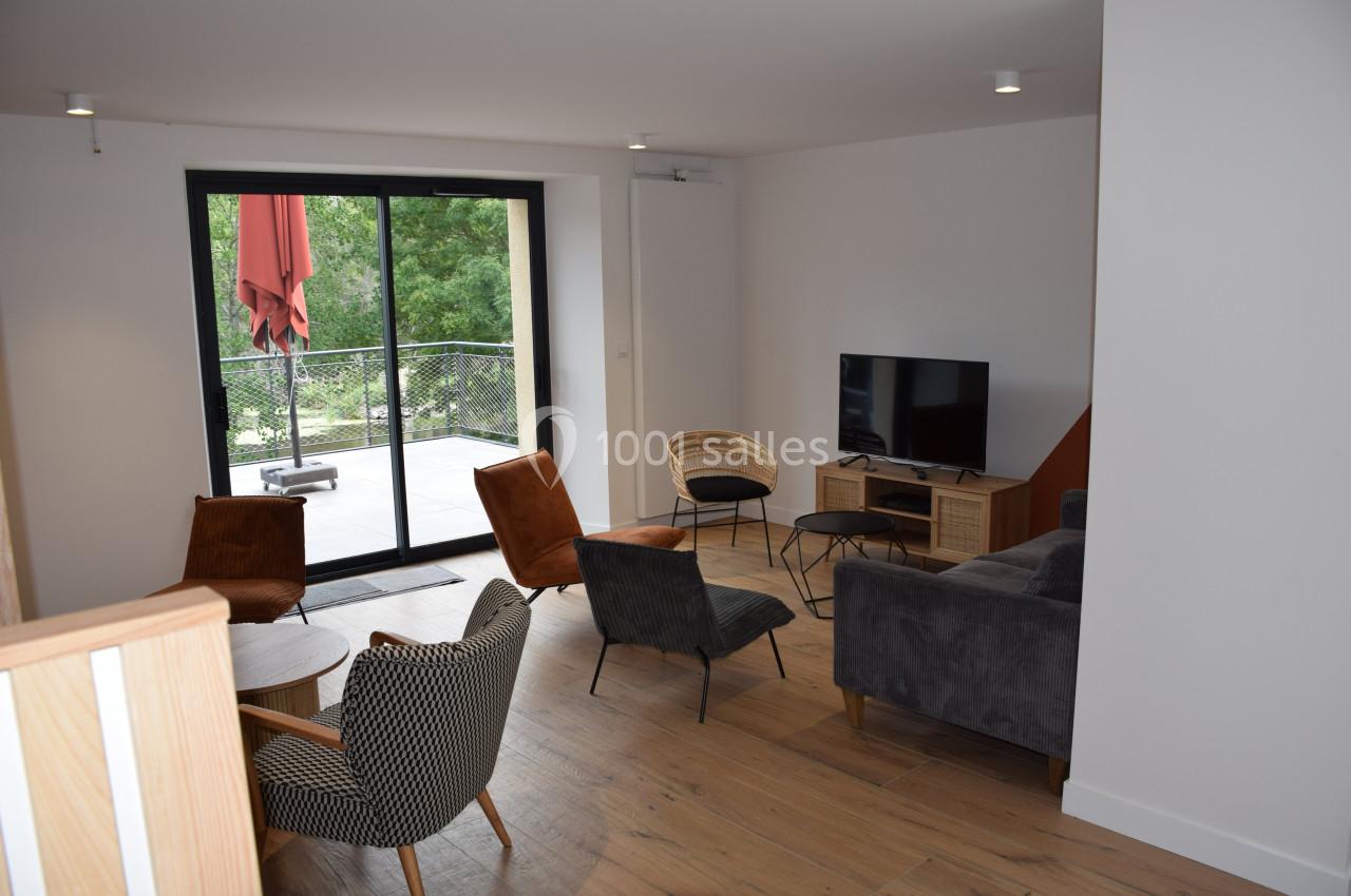 Salon moderne avec parquet, mobilier varié, télévision et grande baie vitrée donnant sur une terrasse arborée.