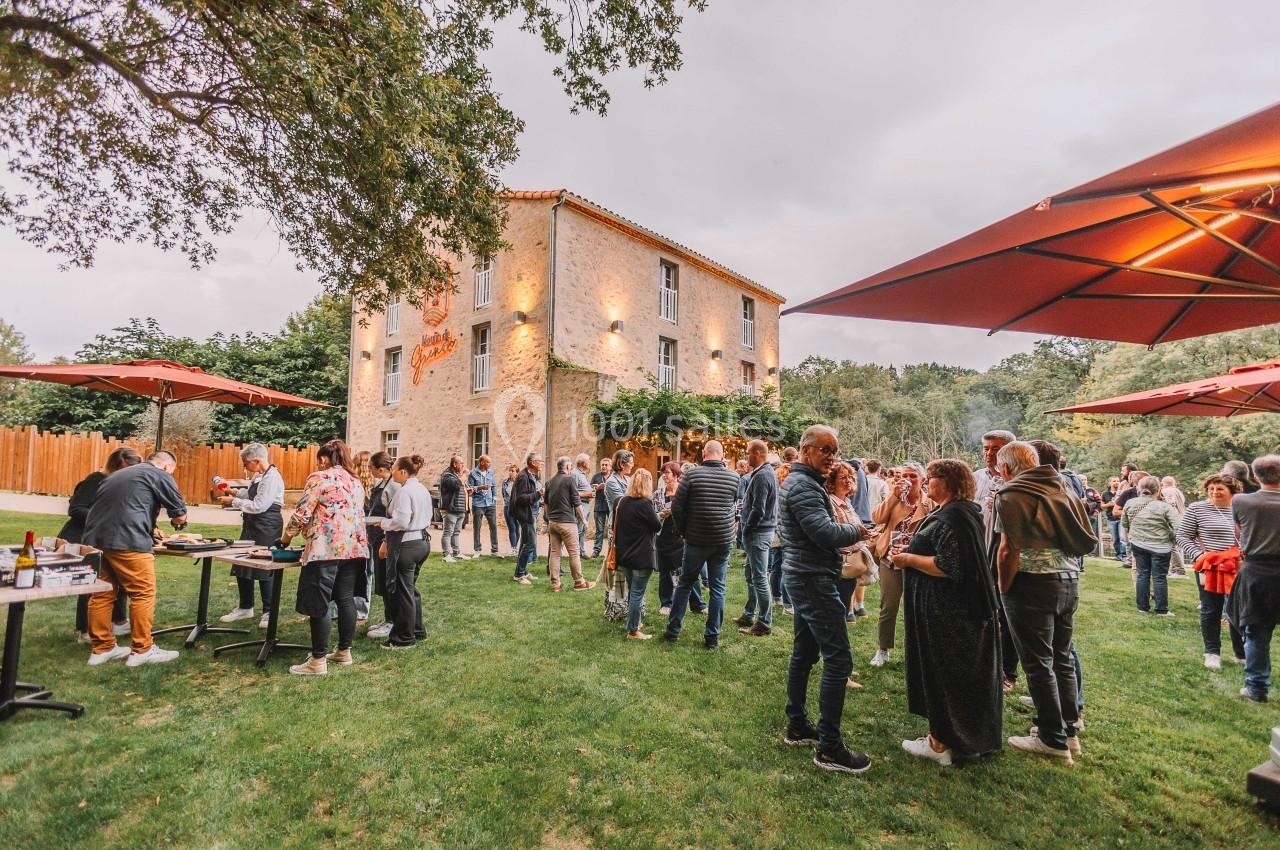 Groupe de personnes réunies dans un jardin devant une maison en pierre, entourées de parasols rouges.