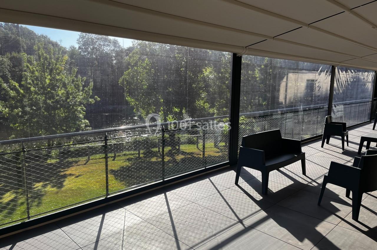 Terrasse couverte avec mobilier moderne, offrant une vue sur un espace vert et des arbres ensoleillés.