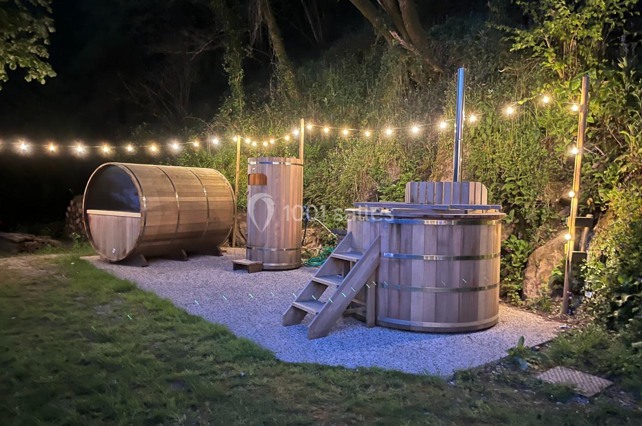 Bains nordiques en bois et sauna extérieur éclairés par des guirlandes lumineuses dans un jardin de nuit.