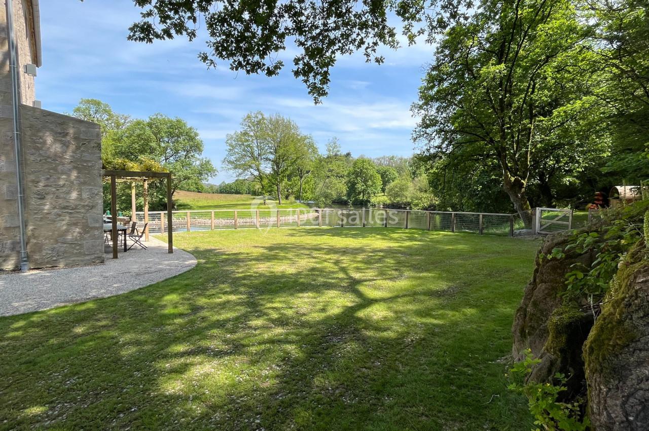 Jardin verdoyant avec pelouse, arbres et clôture en bois, partiellement ombragé par des branches d'arbres.