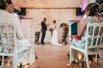 Groupe de personnes rassemblées sur une terrasse en bord de rivière, entourée de verdure et décorée de guirlandes lumineuses.