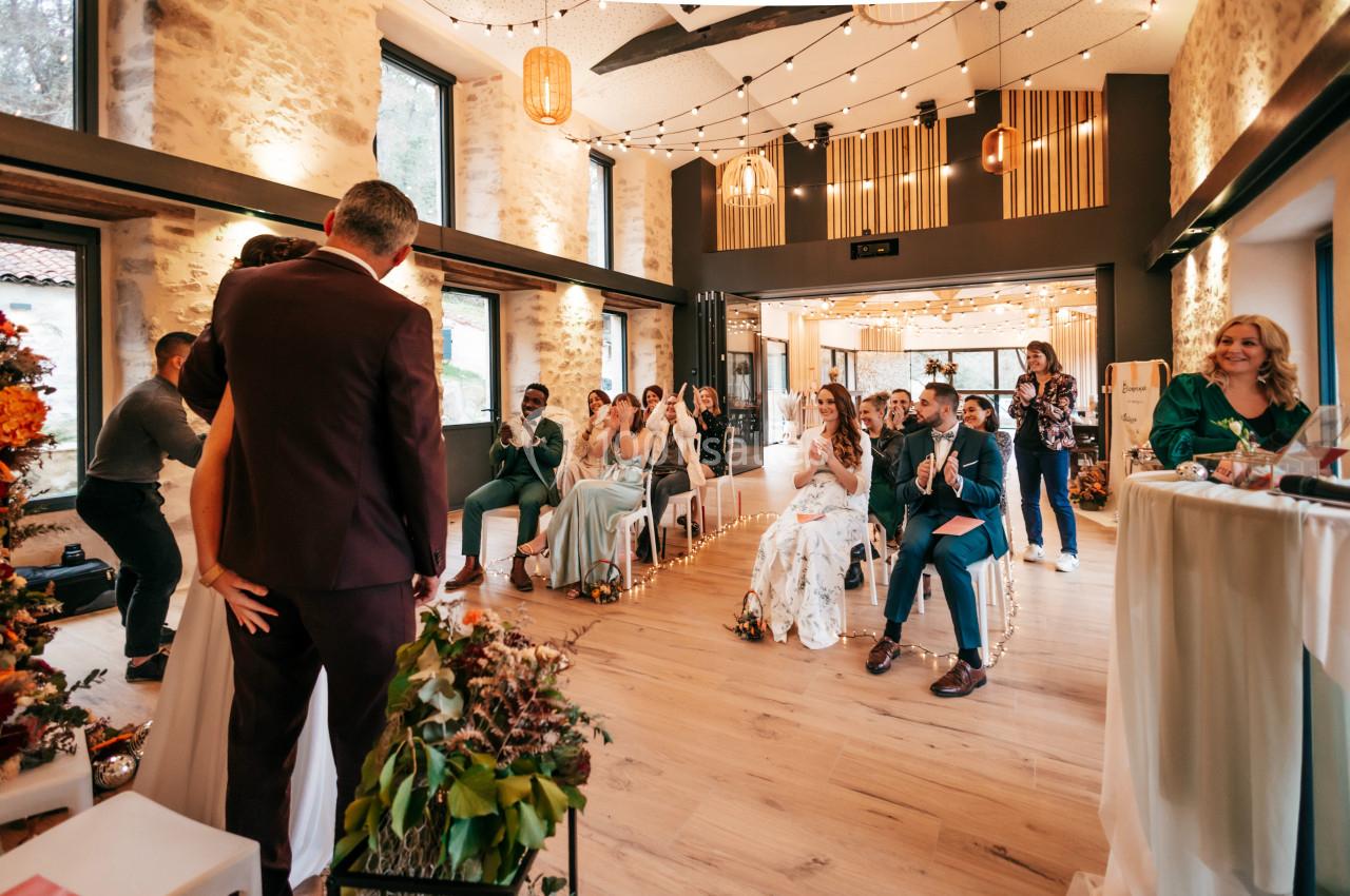 Un couple se marie dans une salle lumineuse, entouré d'invités assis applaudissant avec joie.
