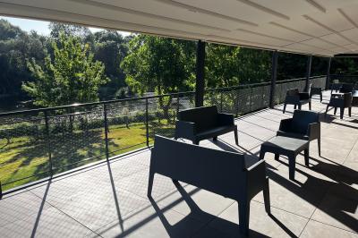 Groupe de personnes rassemblées sur une terrasse en bord de rivière, entourée de verdure et décorée de guirlandes lumineuses.