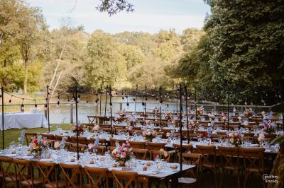 Groupe de personnes rassemblées sur une terrasse en bord de rivière, entourée de verdure et décorée de guirlandes lumineuses.