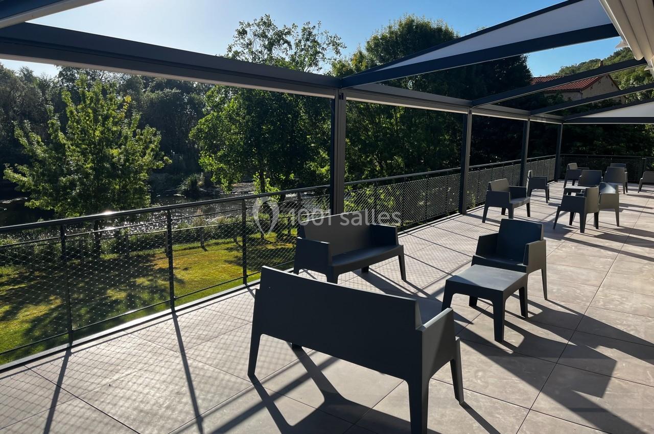 Terrasse ensoleillée avec mobilier moderne, offrant une vue sur un jardin verdoyant et un cours d'eau.