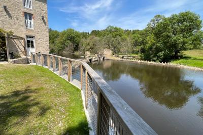 Groupe de personnes rassemblées sur une terrasse en bord de rivière, entourée de verdure et décorée de guirlandes lumineuses.