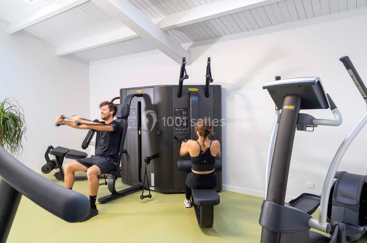 Un homme et une femme utilisent des équipements de musculation dans une salle de sport lumineuse.