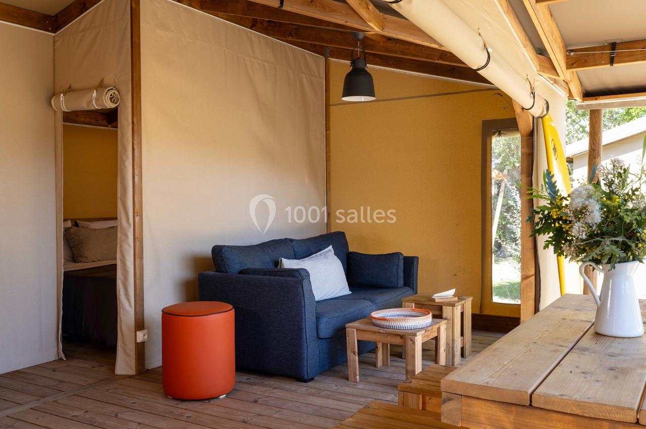 Intérieur d'une tente aménagée avec canapé, table basse, table en bois et bouquet de fleurs, éclairée par la lumière…