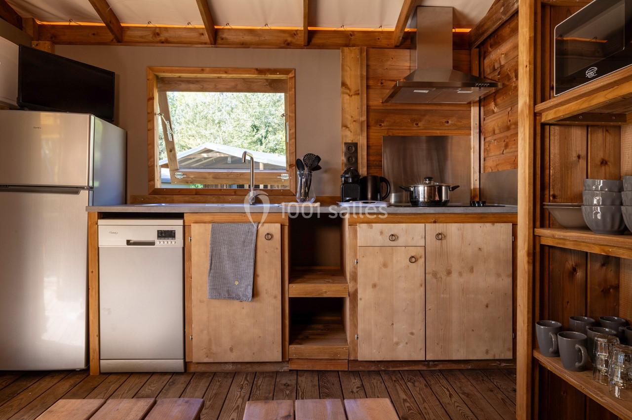 Cuisine en bois avec électroménagers modernes, fenêtre donnant sur l'extérieur et étagères contenant des tasses.