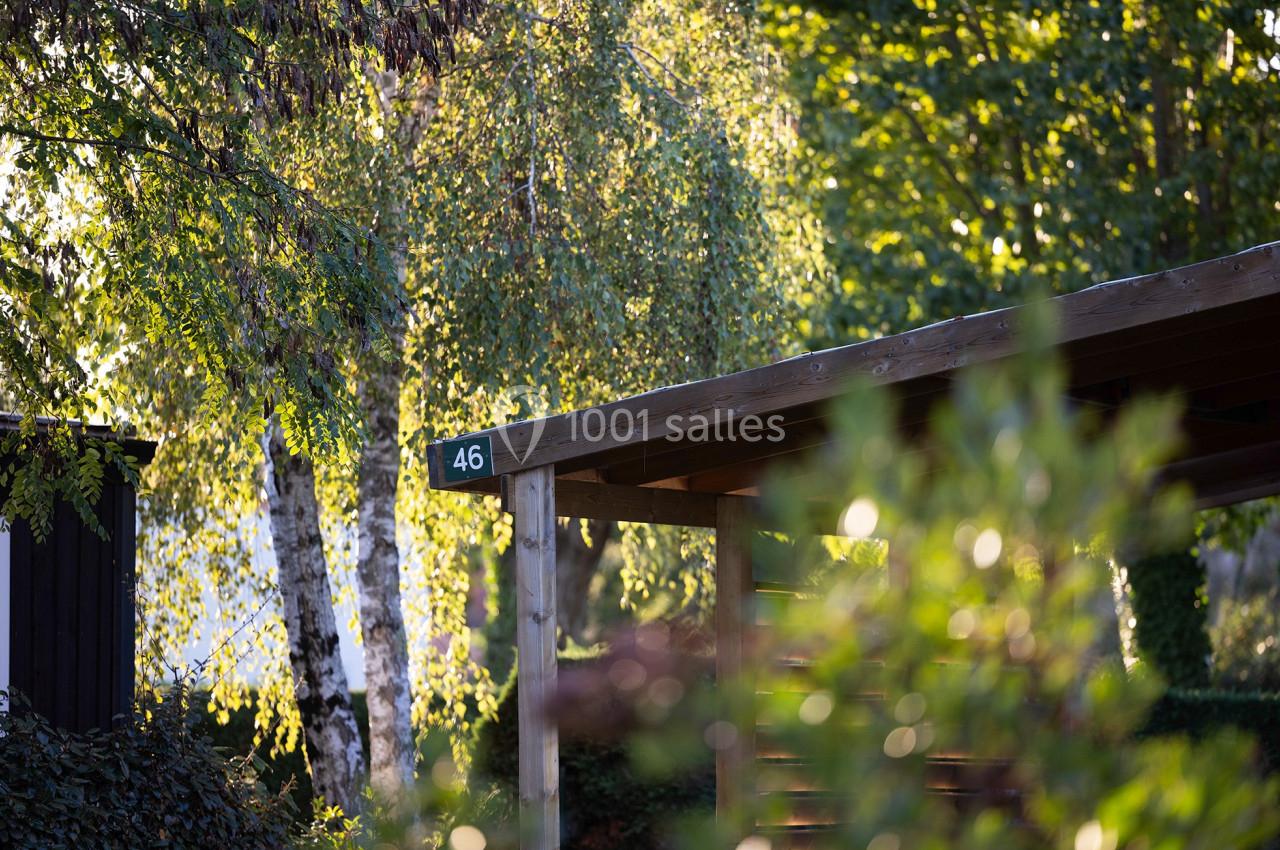 Abri en bois avec un panneau ’46’, entouré de végétation et d'arbres sous une lumière naturelle.