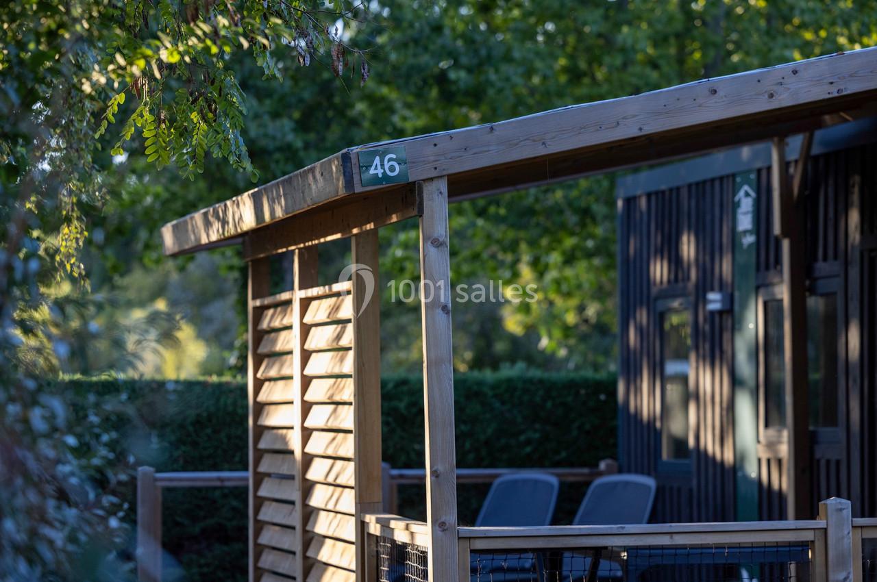 Terrasse en bois avec un numéro 46, entourée de verdure et partiellement ombragée par des arbres.