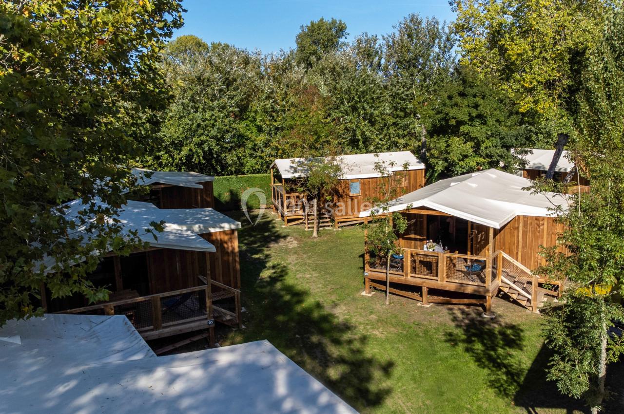 Vue aérienne de plusieurs cabanes en bois avec terrasses, entourées d'arbres et de pelouses verdoyantes.