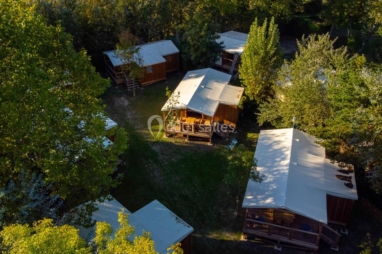Vue aérienne de cabanes en bois entourées d'arbres dans un cadre naturel verdoyant.