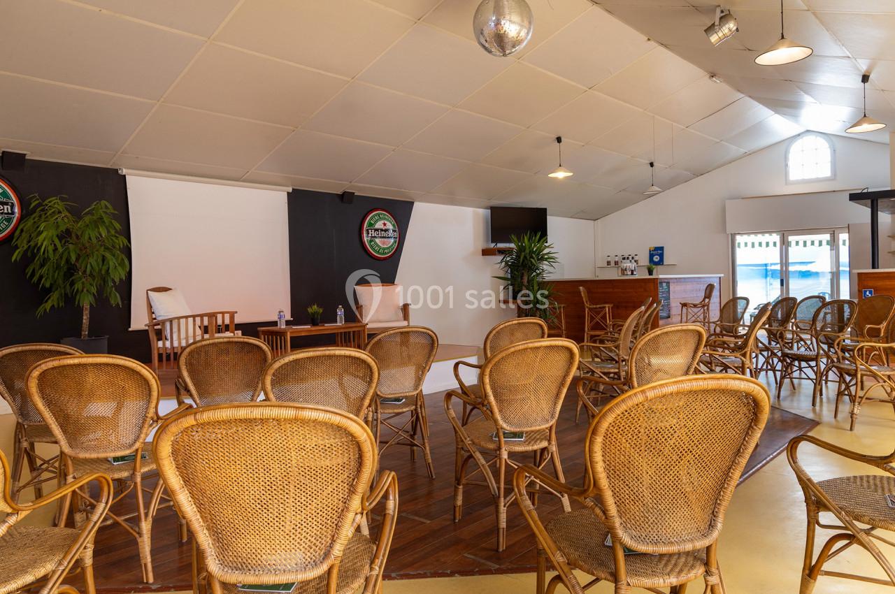 Salle avec des chaises en rotin disposées face à une petite scène, décorée de plantes et éclairée par une lumière naturelle.