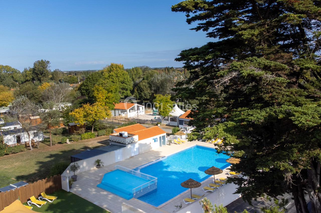 Vue aérienne d'un camping avec piscine, transats, arbres et mobil-homes dans un environnement verdoyant.