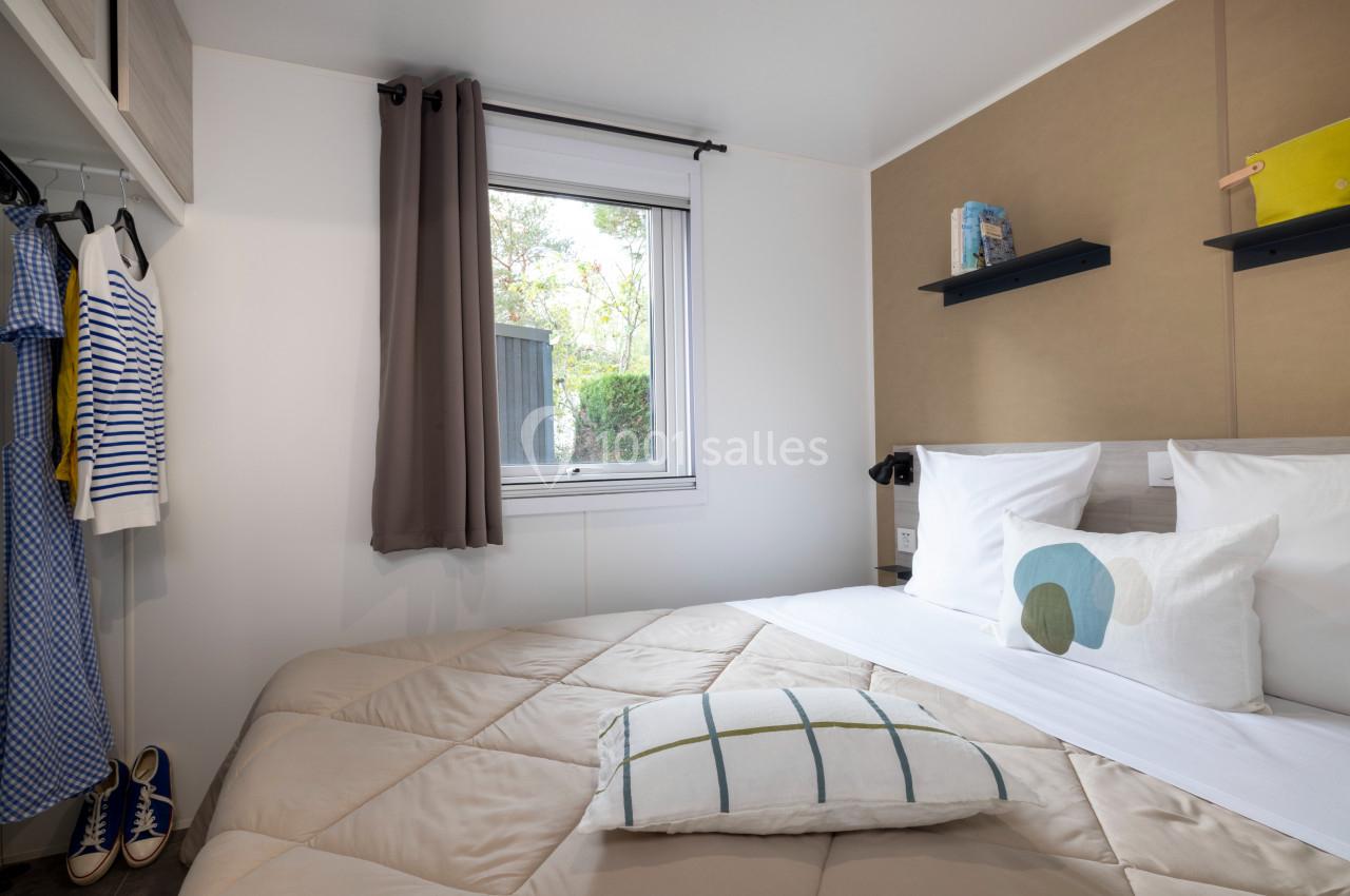 Chambre lumineuse avec lit double, étagères murales, fenêtre donnant sur l'extérieur et vêtements suspendus.