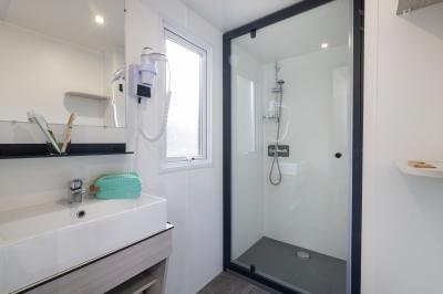 Salle de bain lumineuse avec douche vitrée, lavabo blanc, miroir, et accessoires de toilette.
