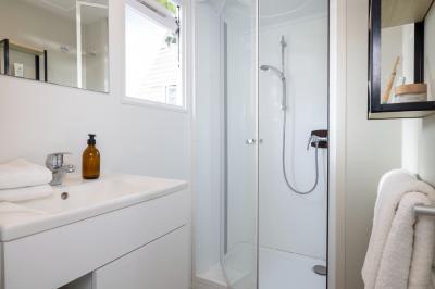 Salle de bain lumineuse avec douche vitrée, lavabo blanc, miroir, et accessoires de toilette.