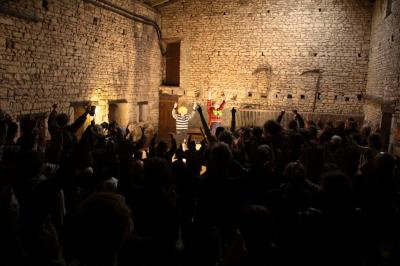 Un spectacle avec deux artistes sur scène dans une salle en pierre, face à un public levant les bras.