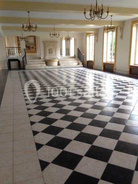 Salle spacieuse avec un sol en damier noir et blanc, des lustres suspendus et des escaliers menant à une estrade.
