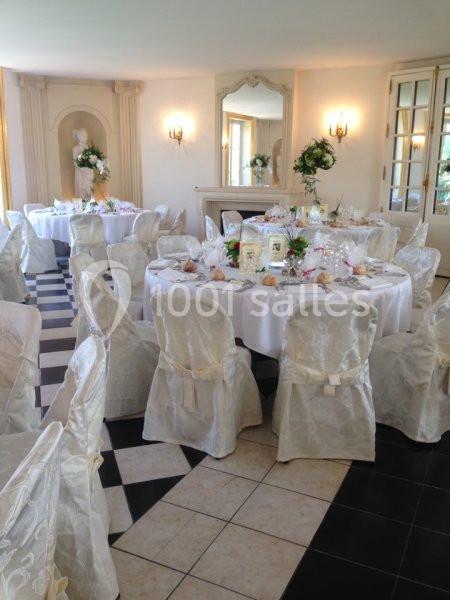 Salle de réception élégante avec tables rondes dressées, nappes blanches et chaises couvertes, décor floral raffiné.