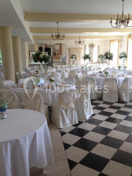Salle de réception élégante avec tables rondes dressées, nappes blanches et décorations florales, sol en damier noir et…