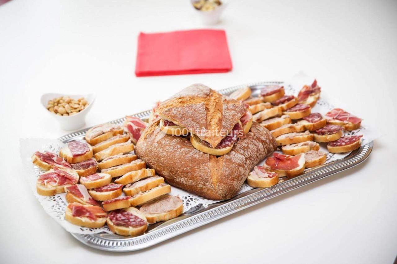 Plateau de toasts garnis de charcuterie et pain artisanal, présenté sur une nappe blanche avec serviette rouge.