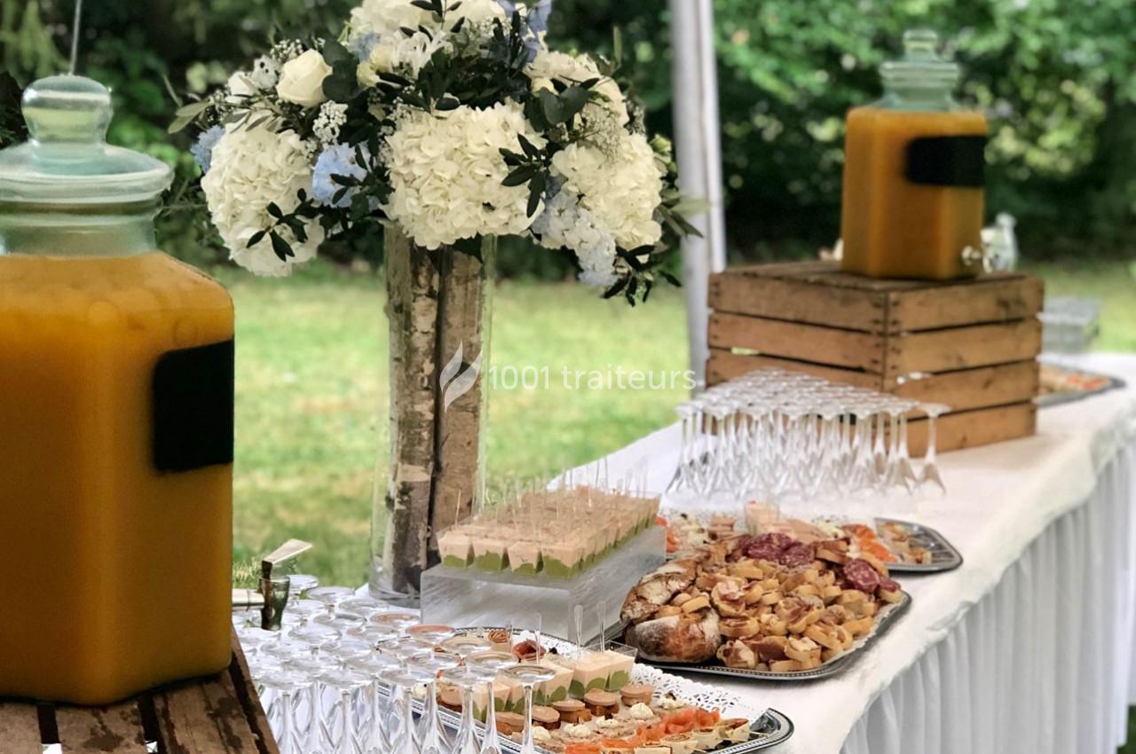 Buffet en extérieur avec boissons, fleurs blanches en décoration et plats variés disposés sur une table blanche.