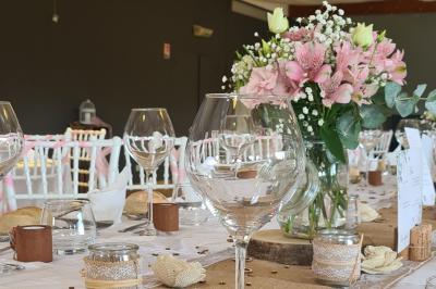 Table décorée pour un événement avec nappes en lin, fleurs roses et blanches, verres à vin et petits pots en verre.