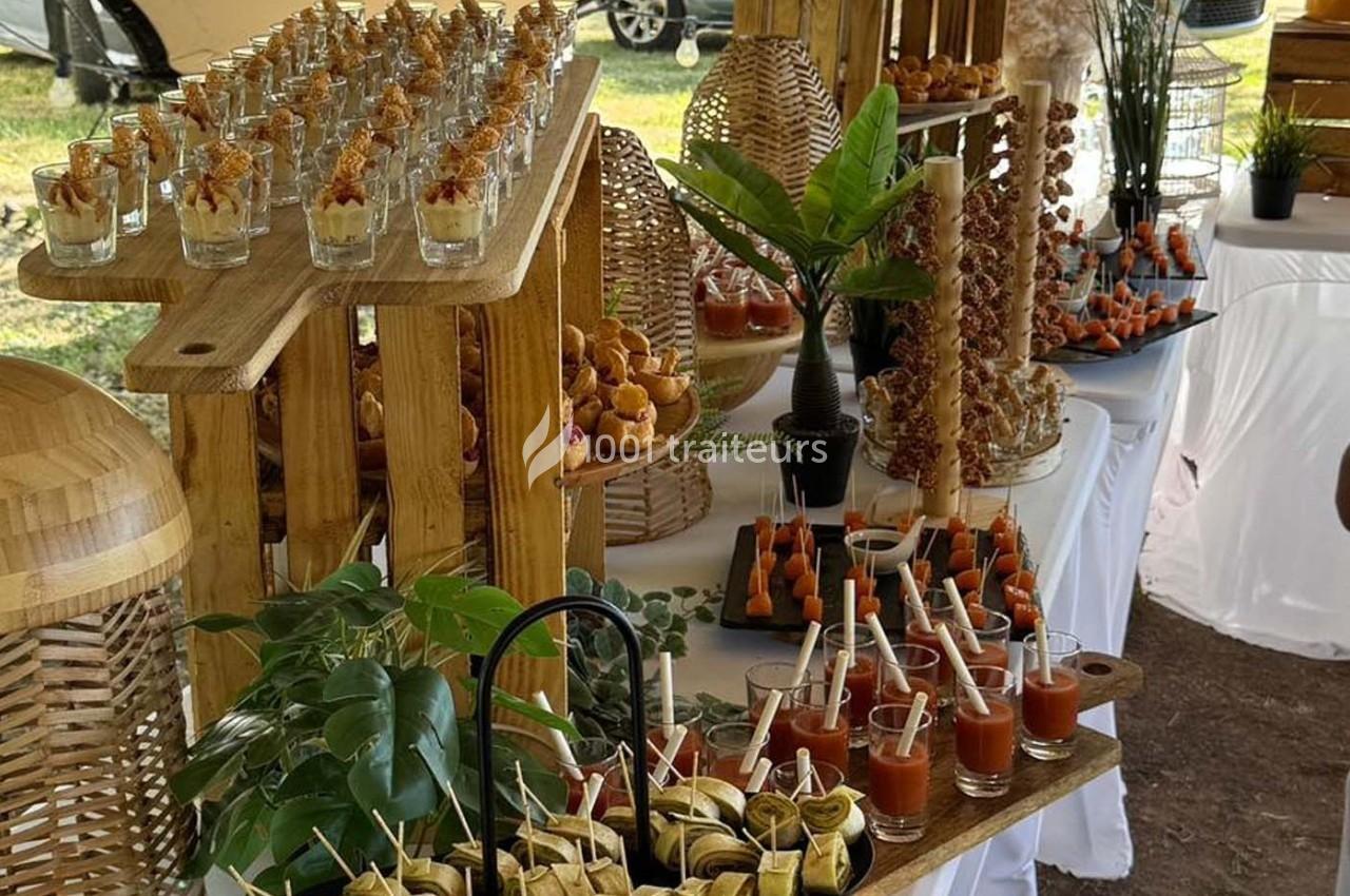 Buffet en plein air avec verrines, brochettes et assortiments de bouchées disposés sur des présentoirs en bois.