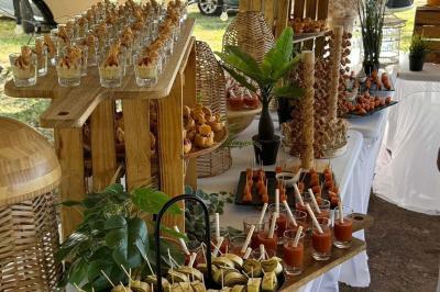 Buffet en plein air avec verrines, brochettes et assortiments de bouchées disposés sur des présentoirs en bois.