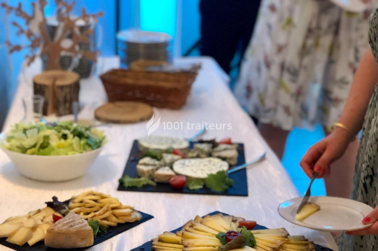 Buffet avec assiettes de fromages variés, salade et pain, une personne se servant une portion.