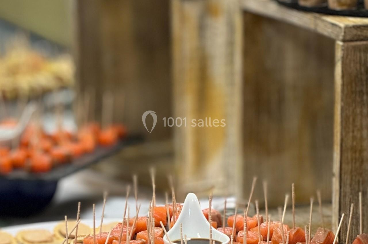 Plateau de bouchées de saumon sur des pics en bois, entouré d'autres amuse-bouches sur une table de réception.