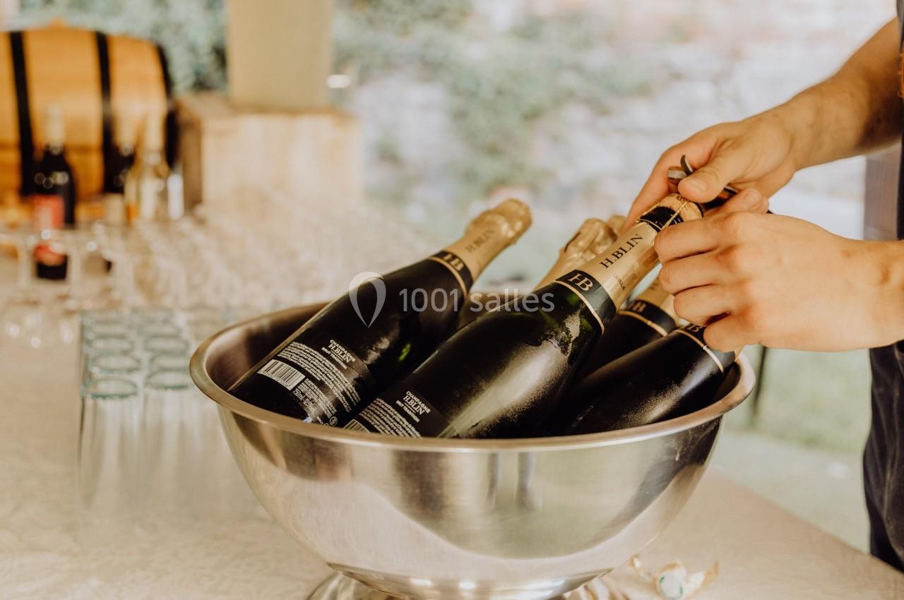 Des bouteilles de champagne dans un seau en métal, avec une personne retirant le muselet d'une bouteille.