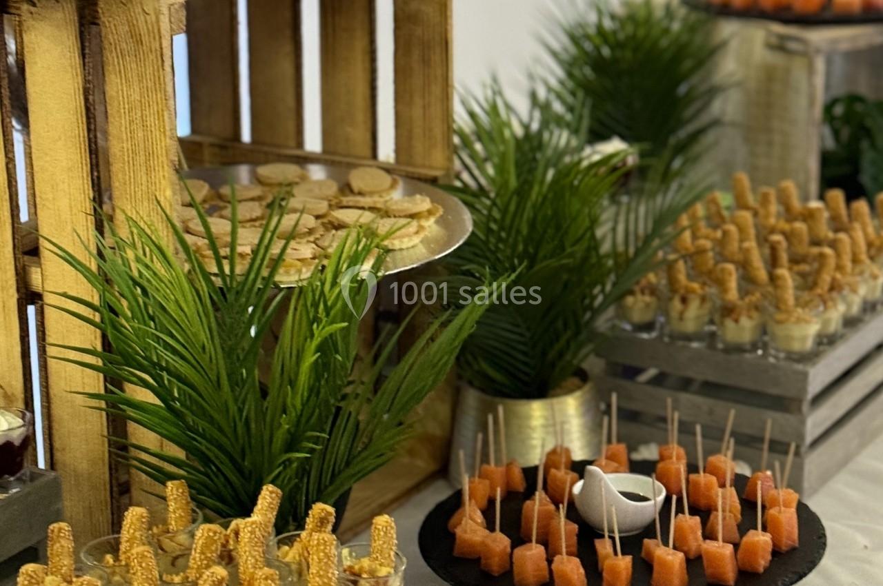 Buffet avec verrines, brochettes apéritives, pains garnis et décorations végétales sur une table blanche.