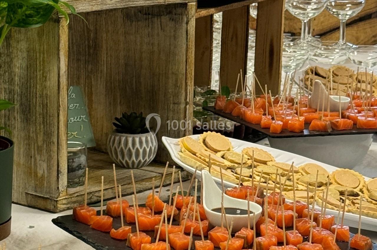 Buffet avec divers amuse-bouches, incluant brochettes de saumon, verrines, toasts et présentoirs en bois rustique.
