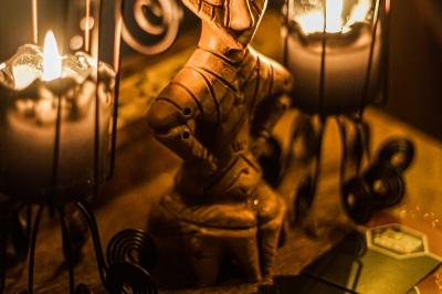 Deux statuettes africaines en gros plan, éclairées par des bougies en arrière-plan dans une ambiance tamisée.