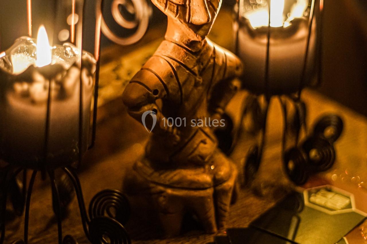 Statue en bois sculptée entourée de bougies allumées et de cartes posées sur une table en bois.