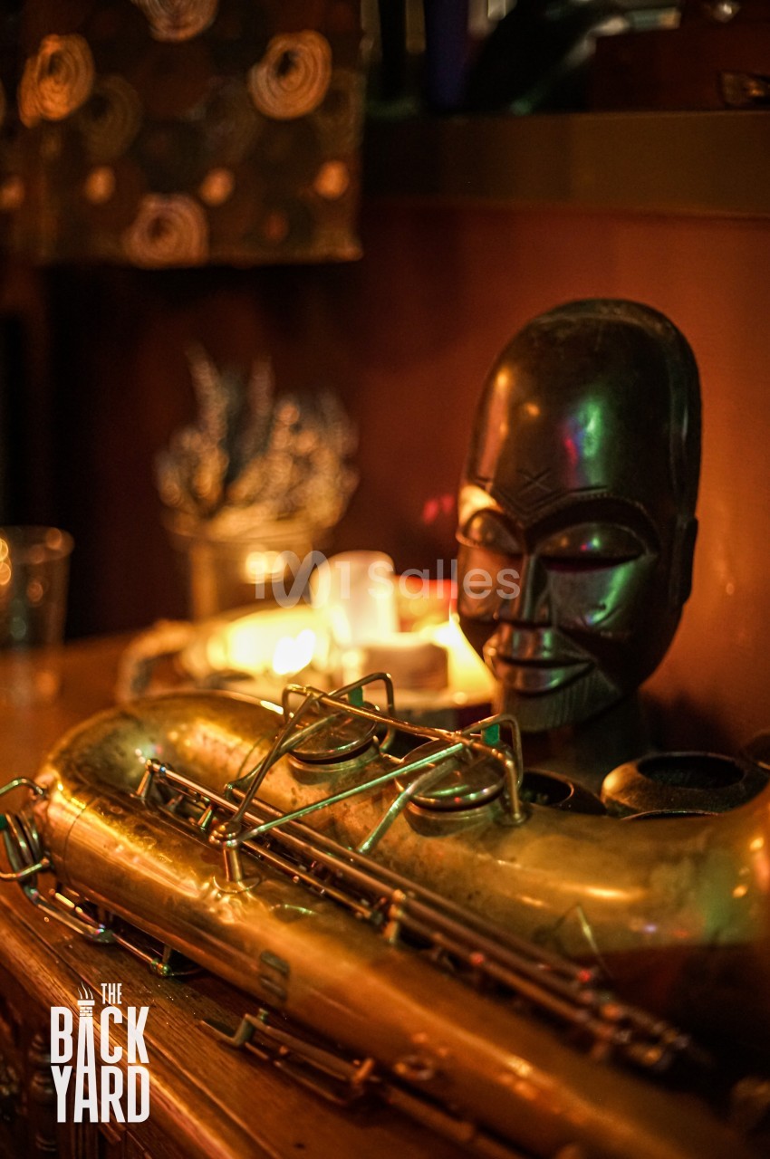 Saxophone doré posé sur une table en bois, avec une sculpture africaine et des bougies en arrière-plan.