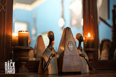 Deux statuettes africaines en gros plan, éclairées par des bougies en arrière-plan dans une ambiance tamisée.