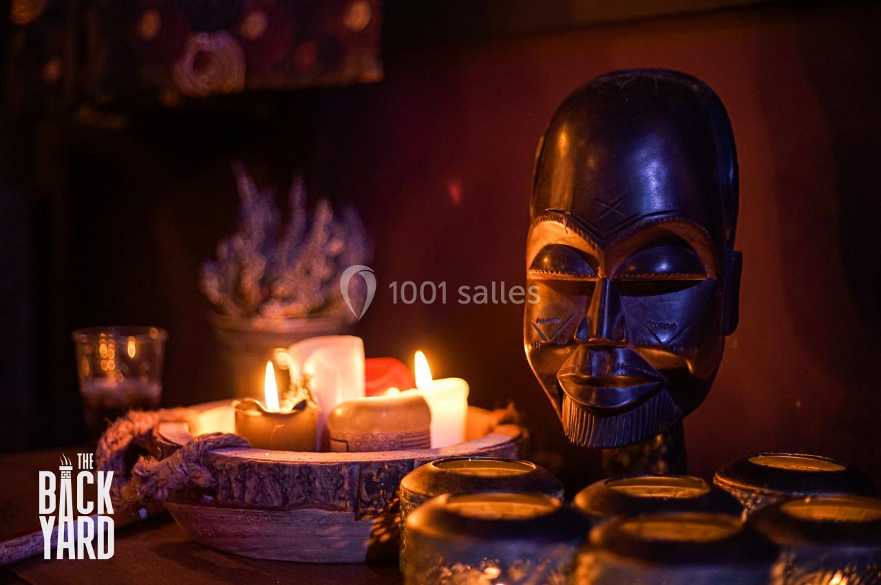 Sculpture en bois d'un visage africain entourée de bougies allumées et d'éléments décoratifs dans une ambiance tamisée.