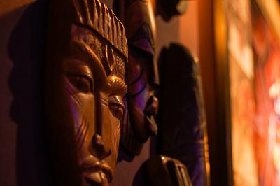 Deux statuettes africaines en gros plan, éclairées par des bougies en arrière-plan dans une ambiance tamisée.