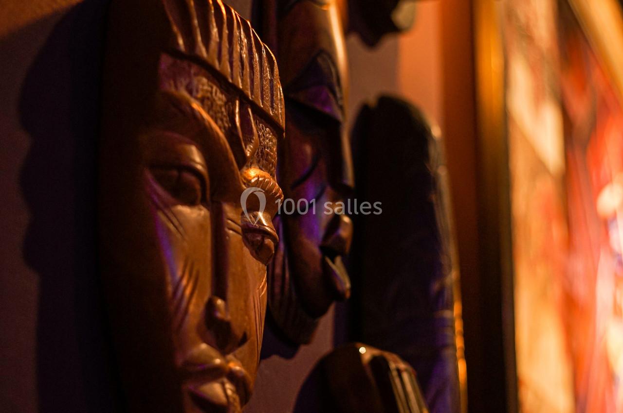 Masques en bois sculpté accrochés à un mur faiblement éclairé, avec une lumière chaude en arrière-plan.