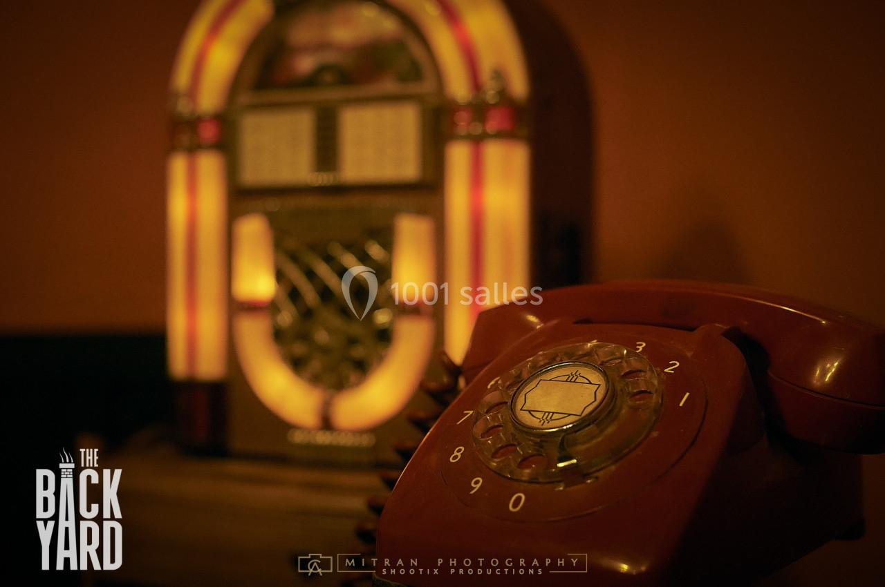 Un téléphone vintage rouge au premier plan avec un jukebox rétro flou en arrière-plan.
