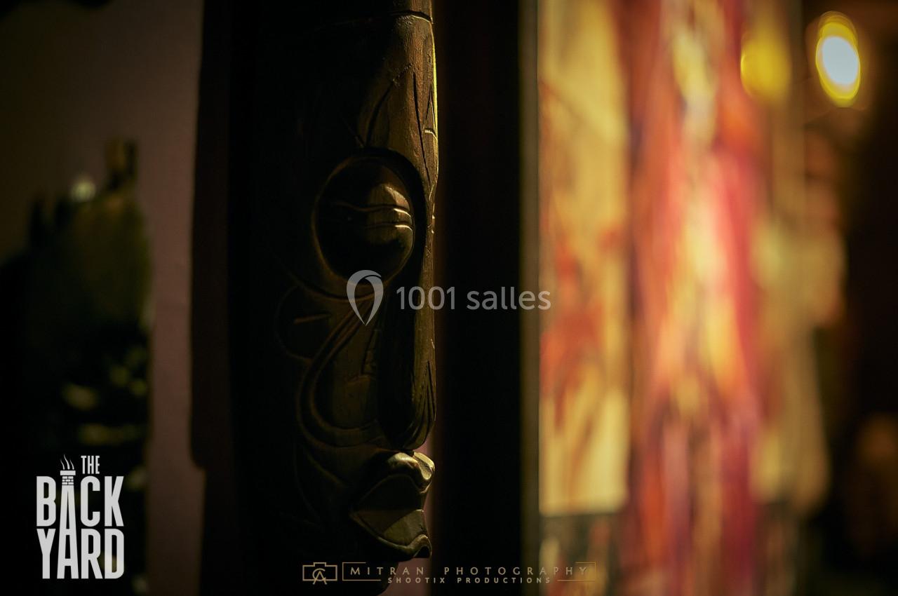 Sculpture en bois sombre avec des motifs gravés, partiellement éclairée dans un environnement tamisé.